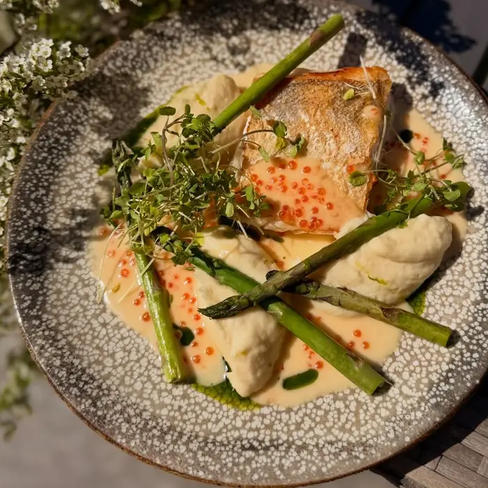Filet ryby z pomarańczową ikrą, szparagami i białym sosem na kamiennym talerzu